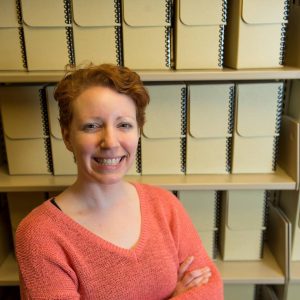 Elizabeth Kelly smiling in front of archival boxes on shelves