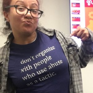 Myrna Morales pointing at her shirt which reads "don't organize with people who use abuse as a tactic."